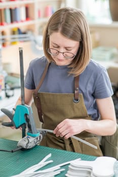 A woman tanner processes the edges of a leather belt in a workshop. Vertical photo