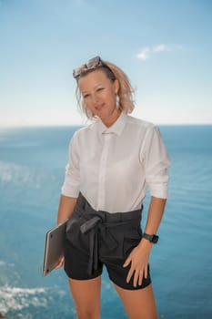 Freelance women sea working on a computer. Pretty middle aged woman with computer and phone outdoors with beautiful sea view. The concept of remote work