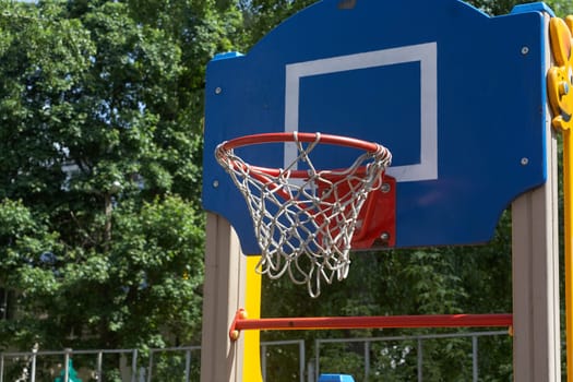 Low angle of basketball hoop with net and backboard against green trees city court