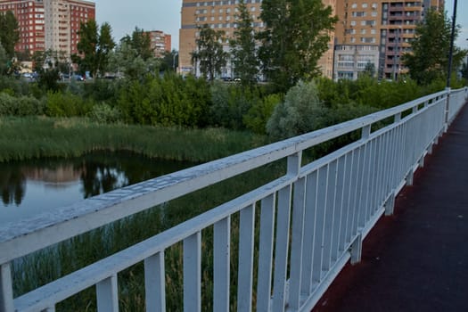 The metal railing of the bridge over the lake. Multi-storey buildings in the background.