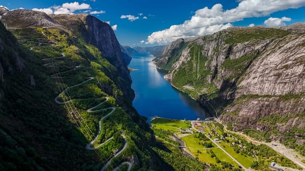 An aerial view of a winding road snaking through the lush green mountainsides, overlooking a serene fjord in Norway on a beautiful sunny day. Kjerag, Lysebotn, Lysefjorden, Norway