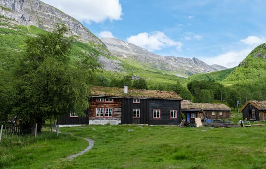 A picturesque view of a traditional Norwegian cabin nestled amongst rolling green hills and majestic mountains. Innerdalen Valley Norway