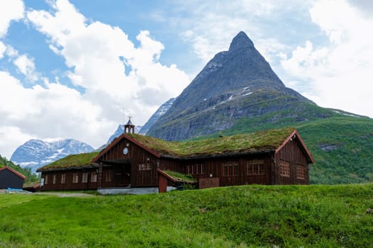 In Norway, a rustic wooden cabin with a grassy roof is nestled among lush green mountains, creating a serene and beautiful landscape. Innerdalen Norway's most beautiful mountain valley