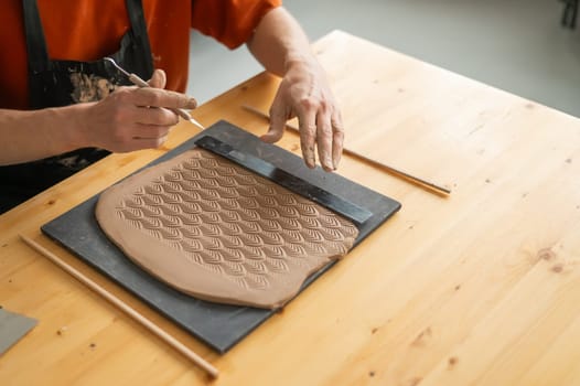 Close-up of a potter's hands cutting off a piece of rolled clay with patterns