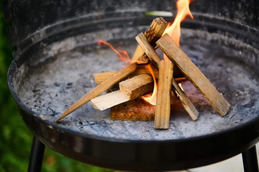 Close-up image showing a fire being started in a barbecue grill with wooden logs, evoking warmth and outdoor enjoyment.