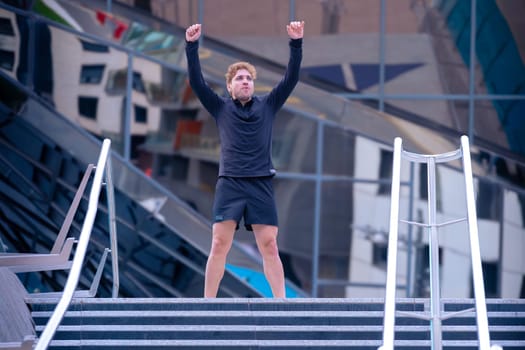 Fit happy man smiling on top of the stairs, celebrating the race victory with his arms raised.