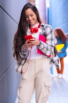 Young smiling student with notebook in hand uses social networks with smartphone applications and wireless technology outdoors.