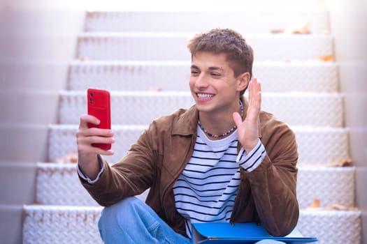 A happy student is on the university campus making a video call with a mobile phone. College life