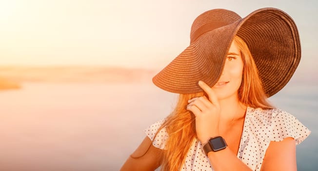 Portrait of happy young woman wearing summer black hat with large brim at beach on sunset. Closeup face of attractive girl with black straw hat. Happy young woman smiling and looking at camera at sea