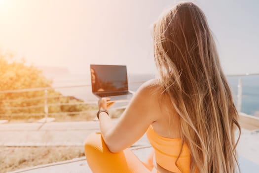 Digital nomad, Business woman working on laptop by the sea. Pretty lady typing on computer by the sea at sunset, makes a business transaction online from a distance. Freelance, remote work on vacation