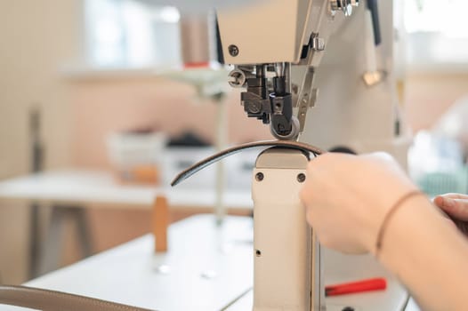 A woman tanner sews a leather belt on a sewing machine. Close-up of hands