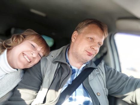 An elderly couple is happily driving through sunny countryside, enjoying their daytime road trip together