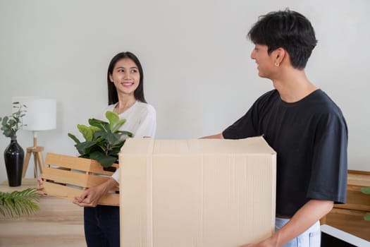 A young couple happily moving into their new house, carrying boxes and plants, symbolizing a fresh start in a modern home.