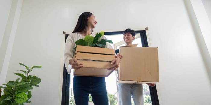 A young couple happily moving into their new house, carrying boxes and plants, symbolizing a fresh start in their modern home.