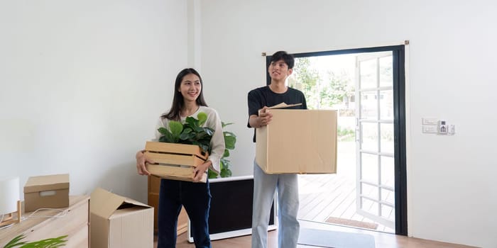 A joyful couple carrying boxes and plants into their new home, symbolizing a fresh start and new beginnings.