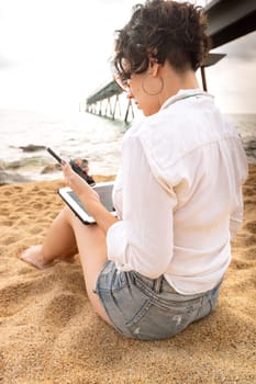 Woman on the beach with digital tablet in hand typing smiling with sunglasses