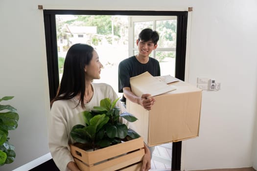 A joyful couple carrying boxes and plants into their new home, symbolizing a fresh start and new beginnings.