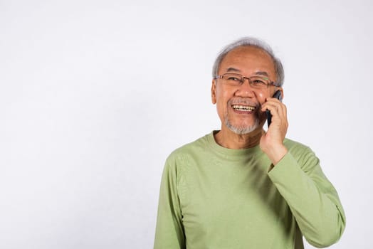 Portrait Asian smiling old man with glasses while talking on his cell phone studio shot isolated on white background, happy senior man calling to someone with mobile phone