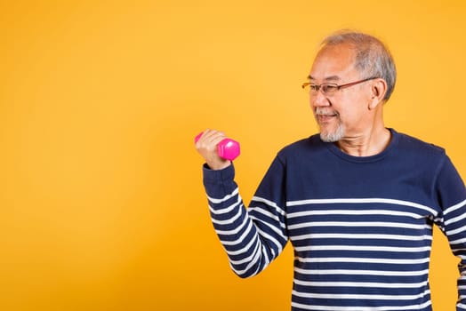 Portrait Asian smiling old man holding a pink dumbbell lifts it with strength and power studio shot isolated yellow background, senior man pensioner, Body care, weight loss lifestyle