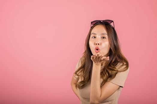 Asian happy portrait beautiful cute young woman teen standing blowing kiss air something on palm hands expresses her love looking to camera studio shot isolated on pink background with copy space