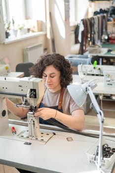 A woman tanner sews a leather belt on a sewing machine. Vertical photo