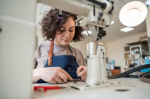 A woman tanner sews a leather belt on a sewing machine