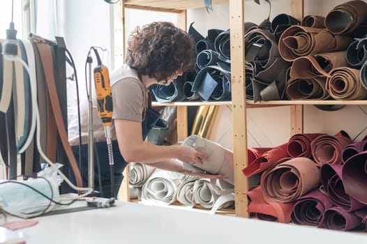 Woman leatherworker selects a roll of leather in the workshop