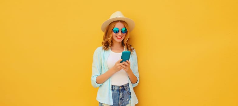 Summer vacation, happy traveler young woman with phone, modern tourist girl looking at smartphone in straw hat on yellow studio background