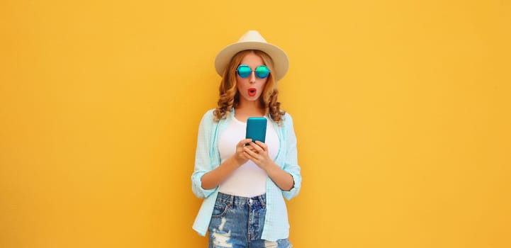 Summer vacation, surprised amazed traveler young woman with phone, shocked tourist girl looking at smartphone in straw hat on yellow studio background