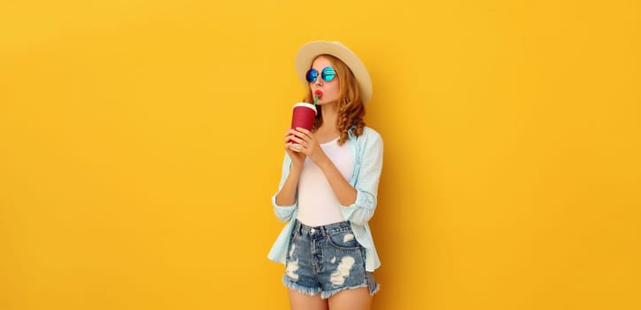 Summer vacation, beautiful modern young woman with cup of coffee, stylish girl drinking fresh juice in tourist straw hat on yellow background