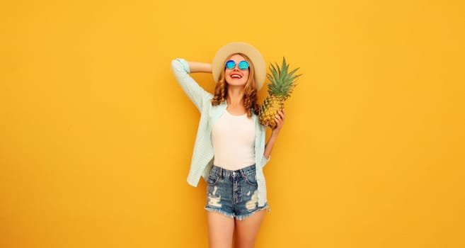 Summer vacation, happy joyful young woman with pineapple fruit in tourist hat, cheerful girl posing on yellow studio background