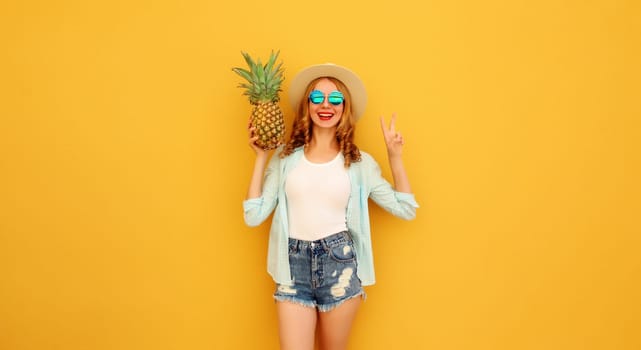 Summer vacation, happy joyful young woman with pineapple fruit in tourist hat, cheerful girl posing on yellow studio background
