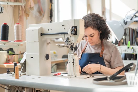 A woman tanner sews a leather belt on a sewing machine