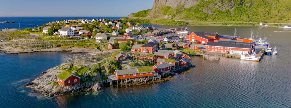 An aerial view of a charming fishing village in Norway, featuring red-roofed houses, boats, and a picturesque coastline. Reine, Lofoten, Norway