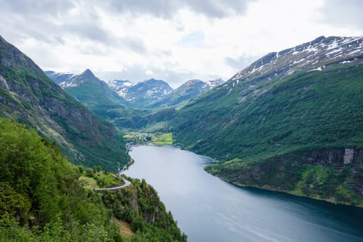 A scenic view of a winding road snaking through the lush green valleys and along the edge of a majestic fjord in Norway. Geiranger fjord Norway