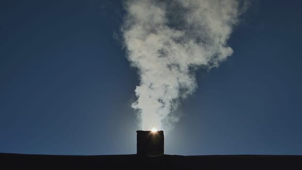 Silhouette of smoke against the sun from the chimney of a village house