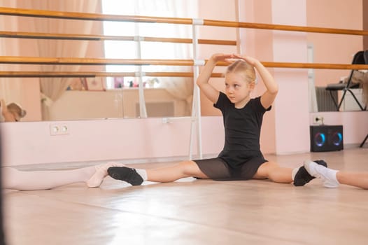 Little girls sit in a circle and do stretching at a ballet school