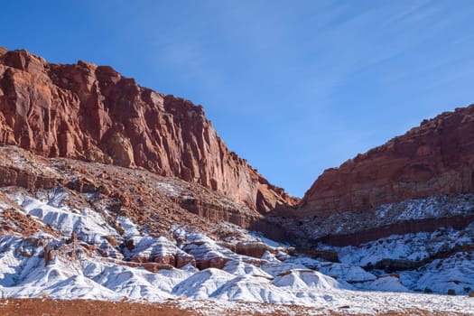 Beautiful winter scene of Capitol Reef in Utah with snow-covered rock formations. The red and white contrast against a clear blue sky showcases nature's beauty. Perfect for nature and travel - Utah