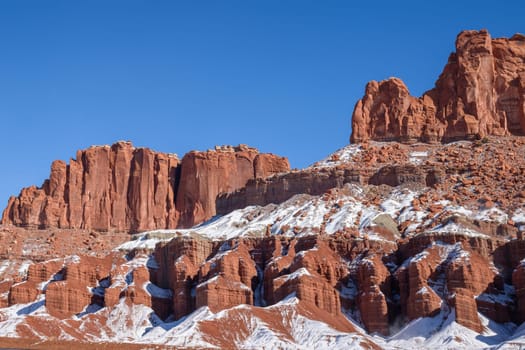 Breathtaking winter landscape showcasing the iconic red rock formations of Capitol Reef National Park in Utah, dusted with snow under a clear blue sky - USA