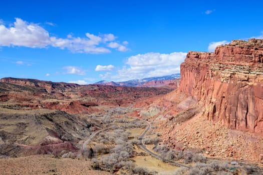 A stunning aerial view of Capitol Reef National Park in the Fruita District orchards, Utah. The image showcases the vibrant red rock cliffs, winding road, and the expansive desert landscape - USA