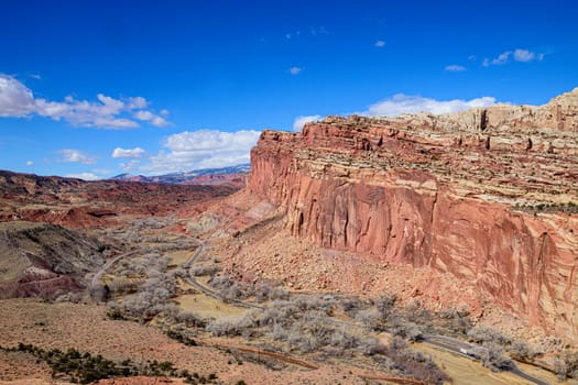 A breathtaking aerial view of the Capitol Reef National Park showcasing the dramatic red rock formations and winding roads of the Fruita District under a vibrant blue sky in Utah - USA
