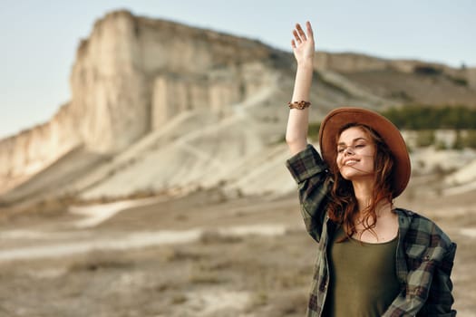 Exhilarated woman in hat celebrating in front of majestic mountain landscape