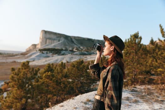 Stylish woman in plaid shirt and hat capturing the moment with vintage camera on sunny day