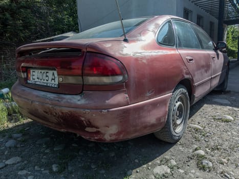 heavily used falling apart neglected car at the sunny summer street of Central Asia in Sokuluk, Kurgyzstan - June 5, 2023