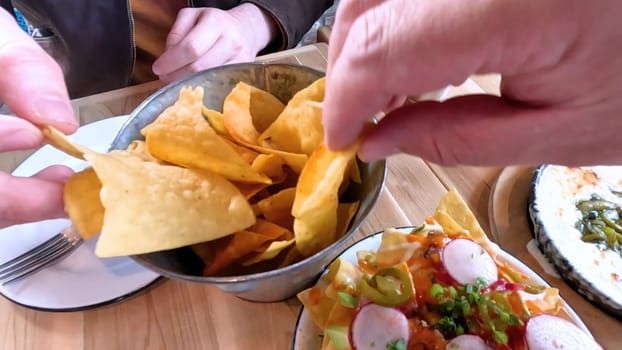 Castle Rock, Colorado, USA-June 12, 2024-Slow motion-Close-up view of a hand picking up a taco from a plate at a restaurant table. The scene features a variety of colorful and appetizing dishes, including nachos topped with cheese and vegetables.