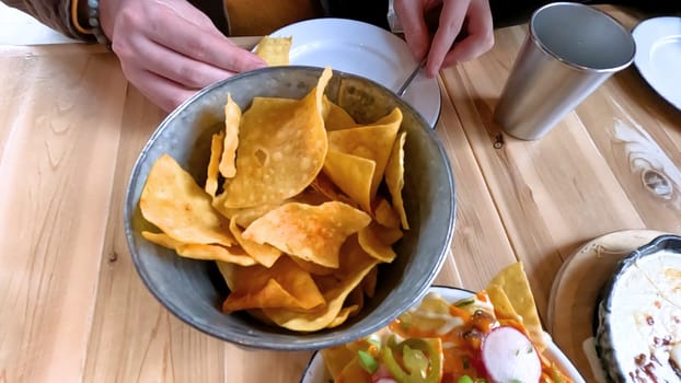 Castle Rock, Colorado, USA-June 12, 2024-Slow motion-Close-up view of a hand picking up a taco from a plate at a restaurant table. The scene features a variety of colorful and appetizing dishes, including nachos topped with cheese and vegetables.