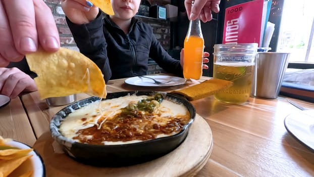 Castle Rock, Colorado, USA-June 12, 2024-Slow motion-Close-up view of a hand picking up a taco from a plate at a restaurant table. The scene features a variety of colorful and appetizing dishes, including nachos topped with cheese and vegetables.