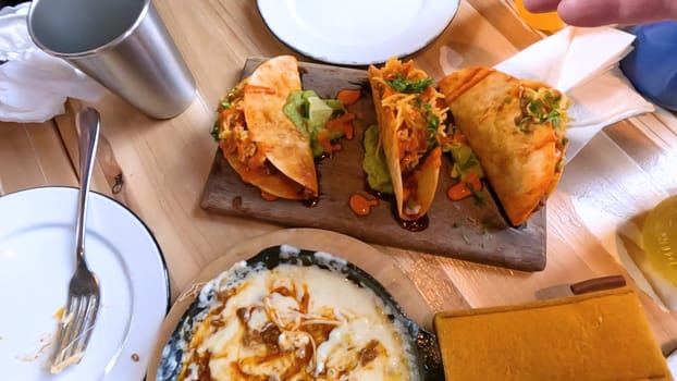 Castle Rock, Colorado, USA-June 12, 2024-Slow motion-Close-up view of a hand picking up a taco from a plate at a restaurant table. The scene features a variety of colorful and appetizing dishes, including nachos topped with cheese and vegetables.