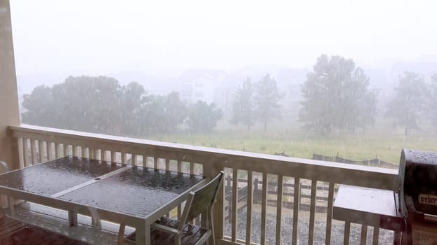 Castle Rock, Colorado, USA-June 12, 2024-Slow motion-Image capturing a hail storm on a wooden deck, highlighting the impact of hail on patio furniture and the deck surface. Hailstones are visible scattered across the wet deck, with patio furniture in the background.