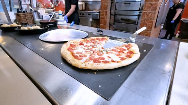 Colorado Springs, Colorado, USA-June 12, 2024-Slow motion-Close-up of a freshly baked pizza slice on a paper plate, placed on a black tray in a pizzeria. The background shows more pizzas being prepared, creating a warm and inviting atmosphere.